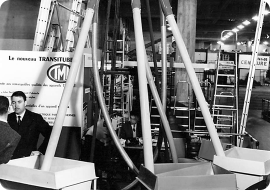 Transitube International trade show stand displaying early flexible screw conveyor systems under the TMM group brand, vintage black and white photo